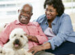 African American couple sitting with their dog with big smiles.