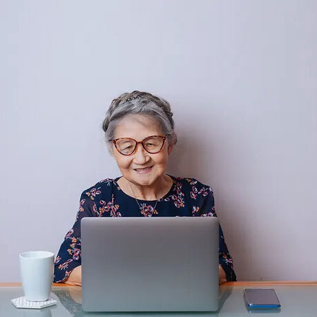 Elderly Asian woman sitting at a table in front of a laptop.